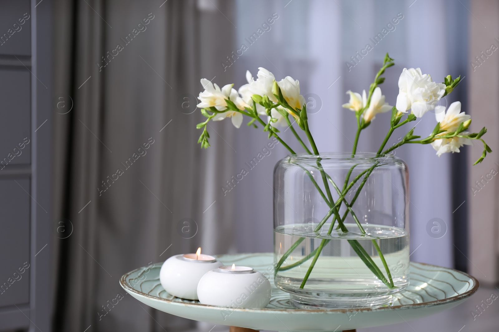 Photo of Vase with beautiful freesia flowers and burning candles on stand indoors, space for text. Interior elements