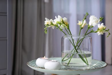 Photo of Vase with beautiful freesia flowers and burning candles on stand indoors, space for text. Interior elements