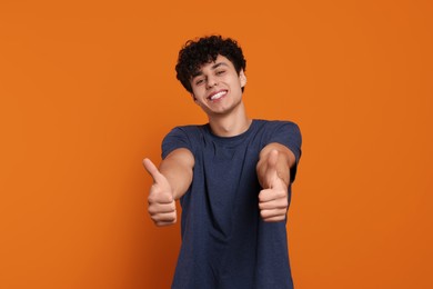 Photo of Handsome young man showing thumbs up on orange background