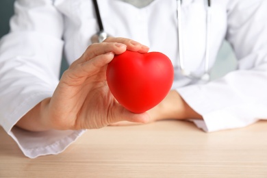 Photo of Doctor holding red heart at wooden table, closeup. Cardiology concept