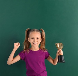 Photo of Happy girl with golden winning cup near chalkboard