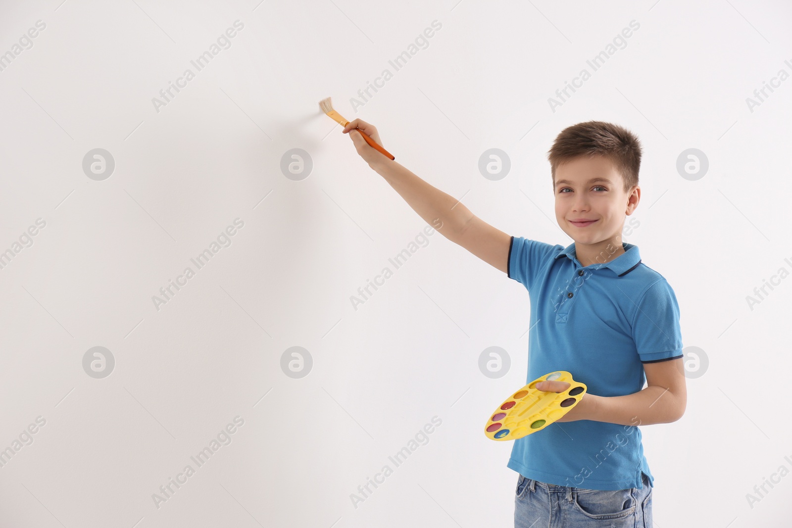 Photo of Little child painting on white wall indoors. Space for text