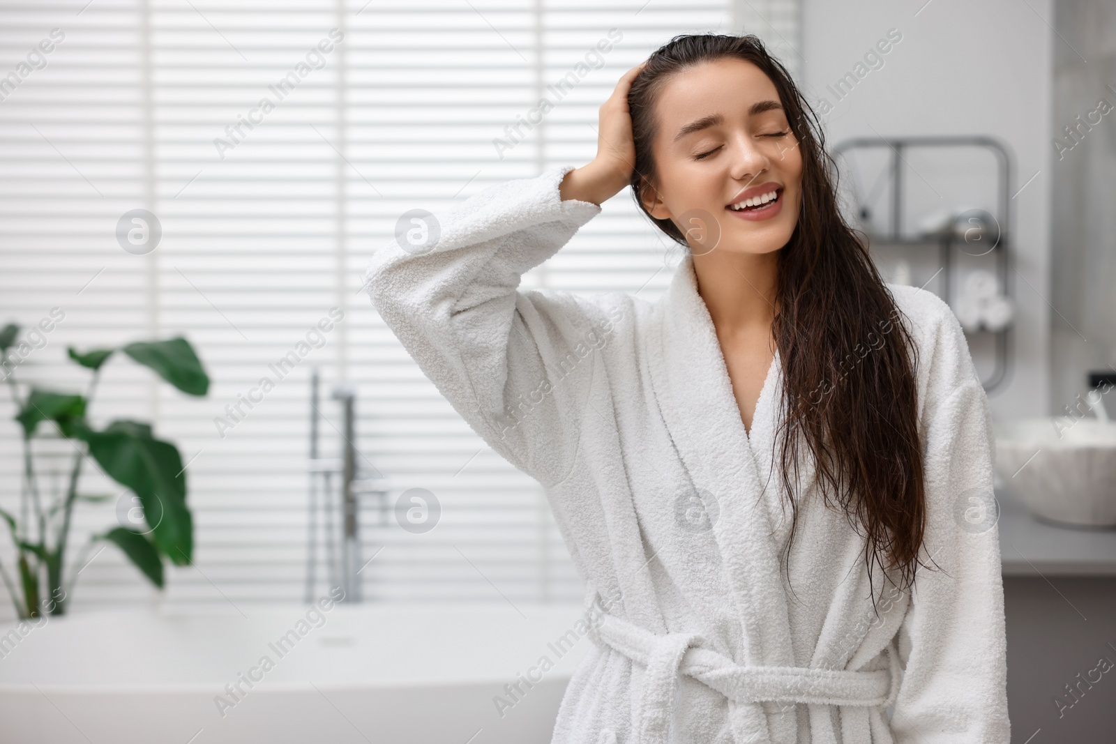 Photo of Smiling woman wearing bathrobe after shower in bathroom. Space for text