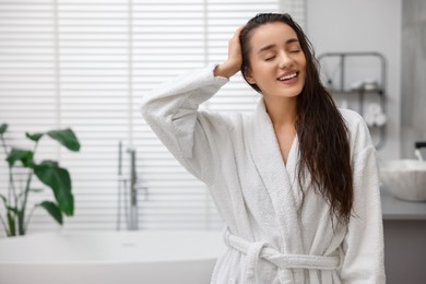 Photo of Smiling woman wearing bathrobe after shower in bathroom. Space for text