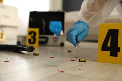 Photo of Investigator in protective gloves working with evidence indoors, closeup. Crime scene