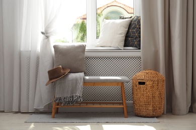 Striped plaid, hat and cushion on bench near window sill with pillows in room. Cozy place to relax