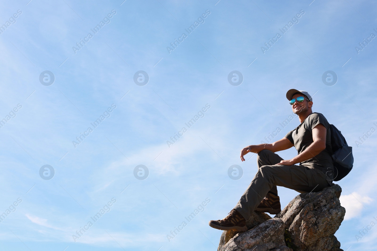 Photo of Man with backpack on rocky peak in mountains. Space for text