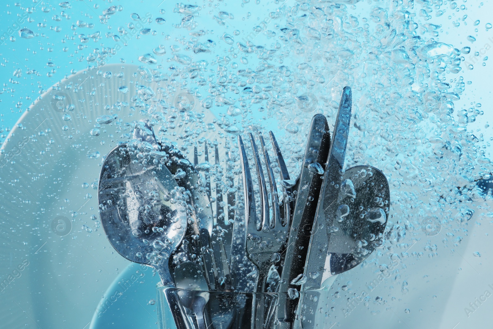 Photo of Washing silver cutlery and plates in water on light blue background