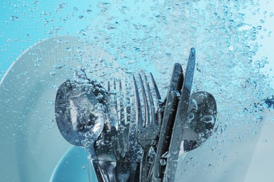 Washing silver cutlery and plates in water on light blue background