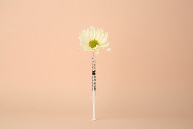 Photo of Medical syringe and chrysanthemum flower on beige background