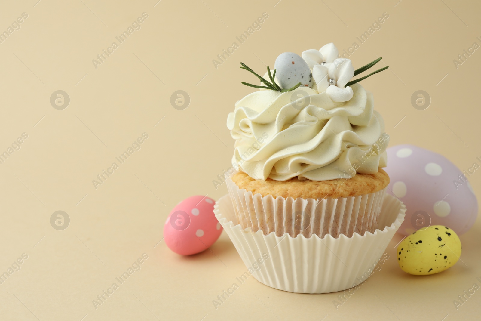 Photo of Tasty Easter cupcake with vanilla cream and candies on beige background, space for text