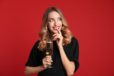 Photo of Happy young woman with glass of champagne on red background. Christmas celebration