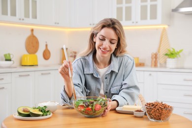 Photo of Woman with salad at wooden table in kitchen. Keto diet