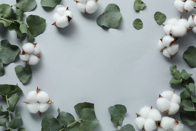 Frame of cotton flowers and eucalyptus leaves on light grey background, flat lay. Space for text