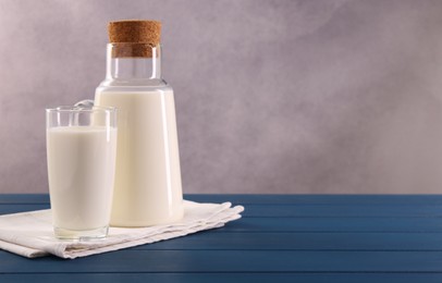 Carafe and glass of fresh milk on blue wooden table, space for text