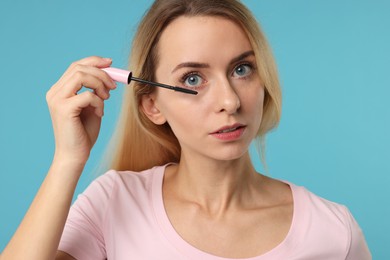 Beautiful woman applying mascara on light blue background, closeup