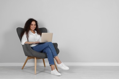 Photo of Young African-American woman working on laptop in armchair indoors. Space for text