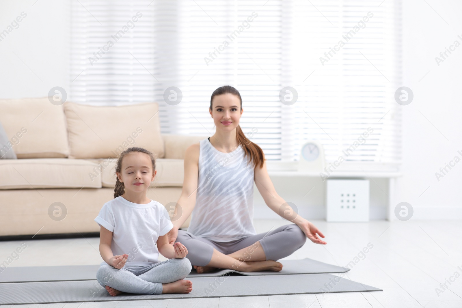 Photo of Young mother with little daughter practicing yoga at home