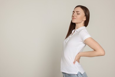 Photo of Young woman suffering from back pain on light grey background, space for text. Arthritis symptoms