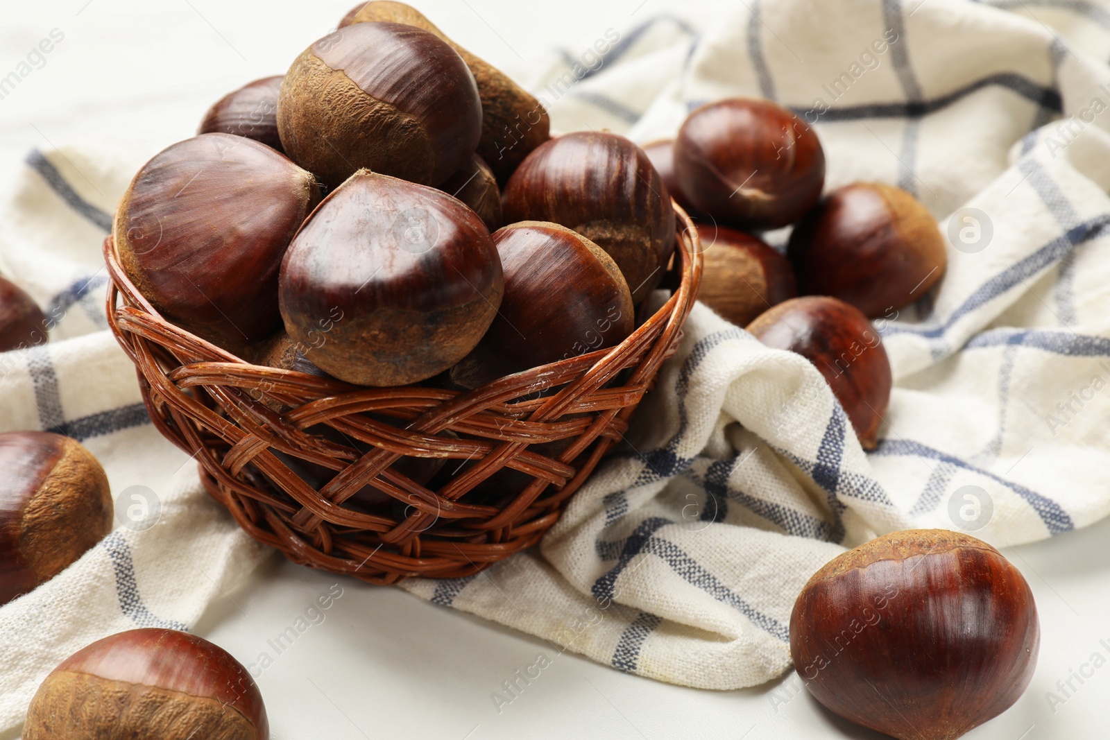 Photo of Sweet fresh edible chestnuts in wicker bowl on white table, closeup