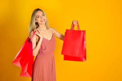 Photo of Happy young woman with shopping bags on yellow background. Black Friday Sale