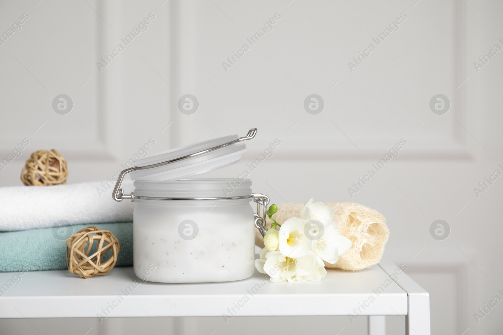 Photo of Jar of salt scrub, freesia flowers and towels on white table. Space for text