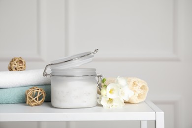 Jar of salt scrub, freesia flowers and towels on white table. Space for text