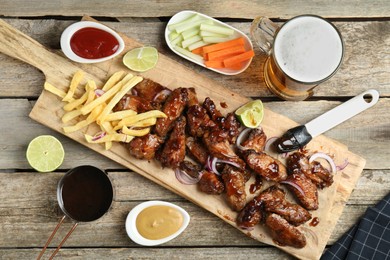 Photo of Tasty roasted chicken wings served with beer on wooden table, flat lay