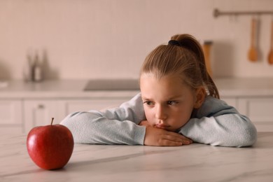 Photo of Cute little girl refusing to eat apple in kitchen