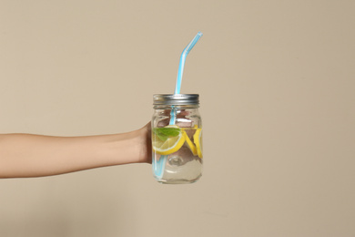 Photo of Young woman holding glass of lemon water on beige  background, closeup