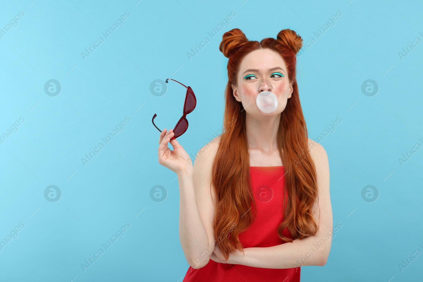 Photo of Beautiful woman with bright makeup blowing bubble gum on light blue background. Space for text