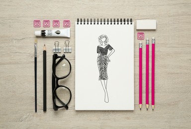 Sketch of stylish clothes in pad on wooden table. Fashion designer's desk with stationery, flat lay