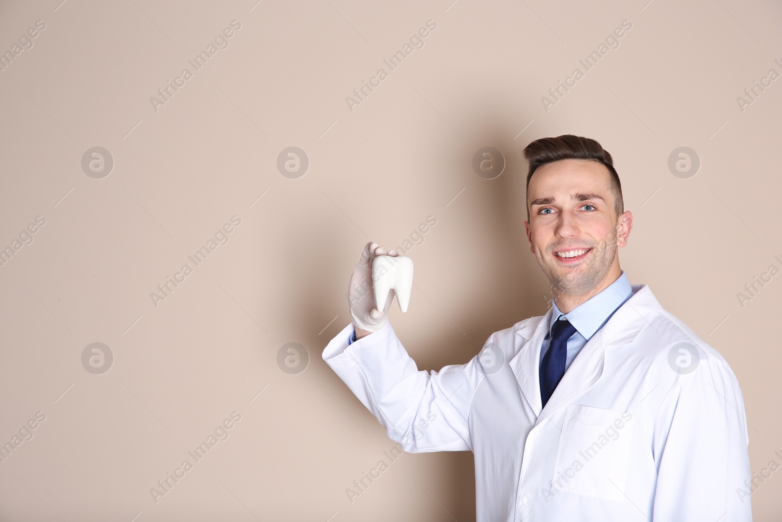 Photo of Male dentist holding tooth model on color background. Space for text