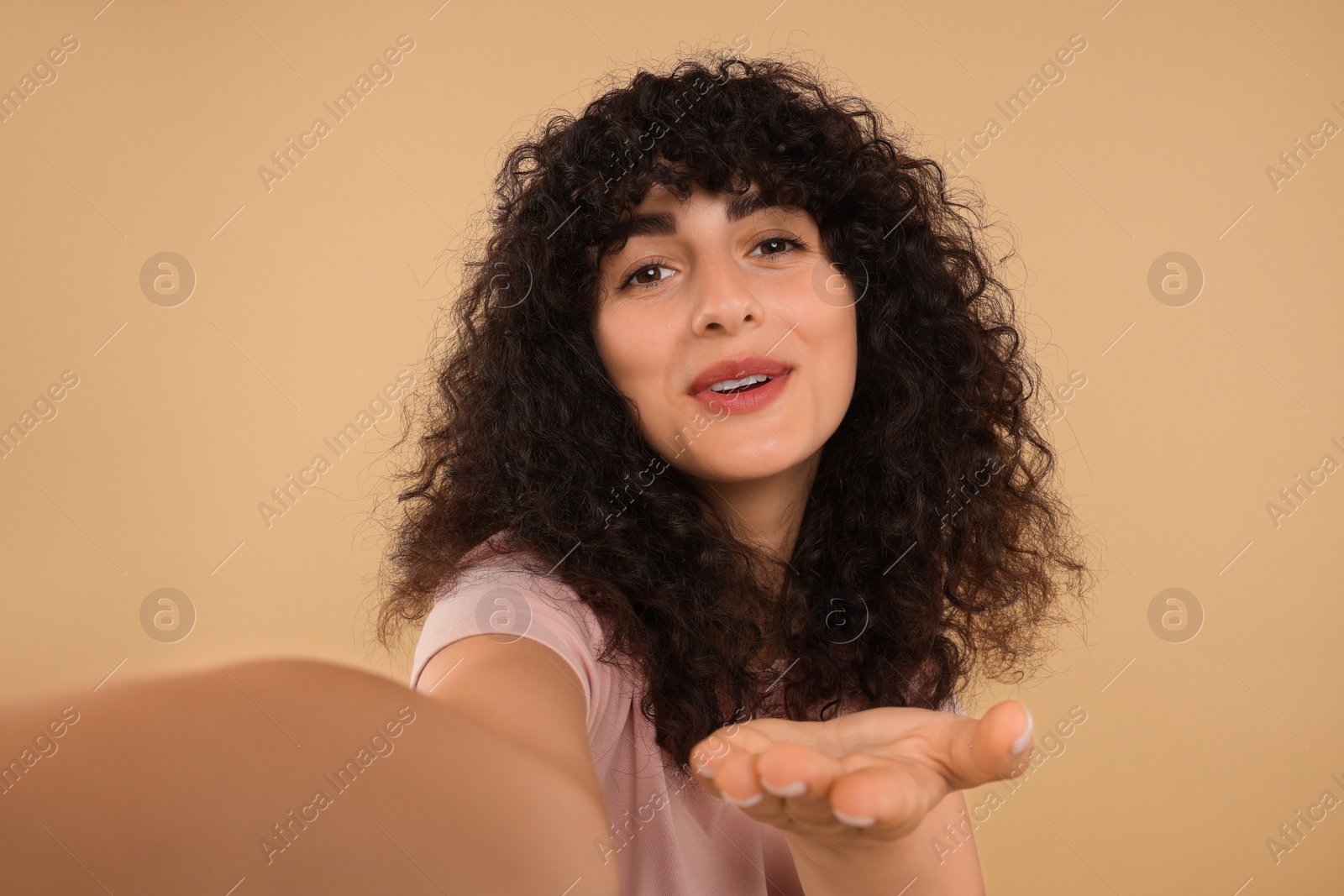 Photo of Happy young woman blowing kiss into camera and taking selfie on beige background