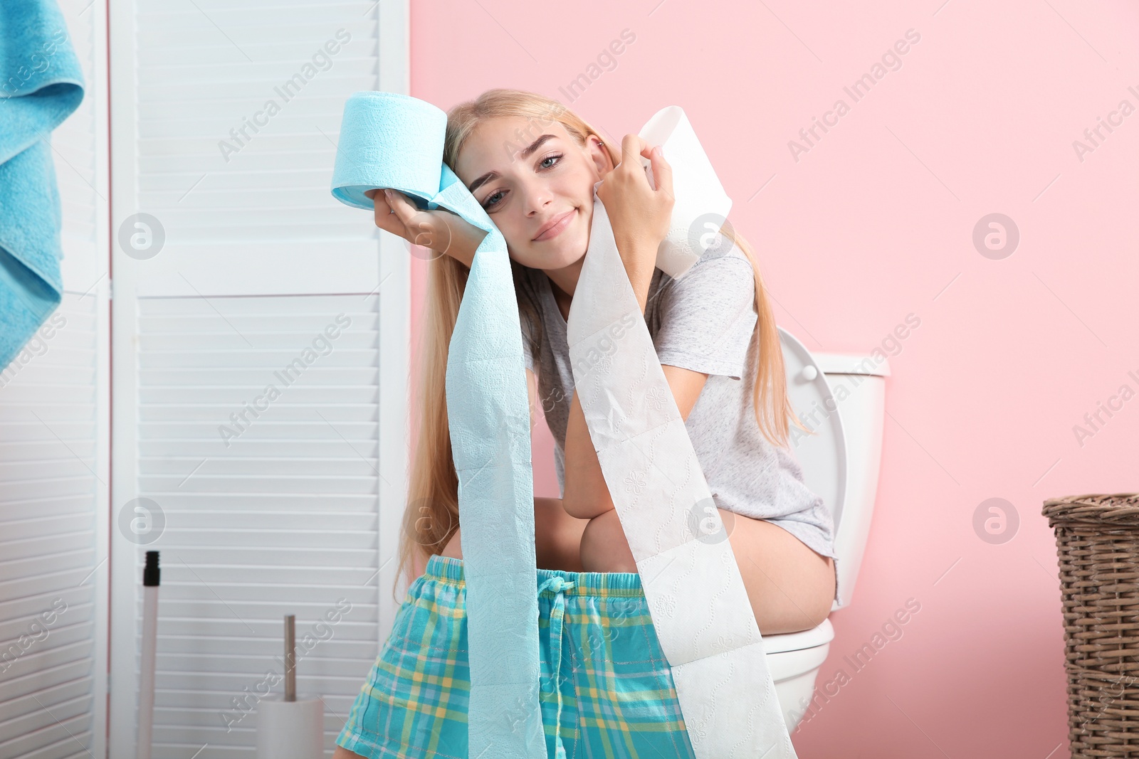 Photo of Woman with paper rolls sitting on toilet bowl in bathroom