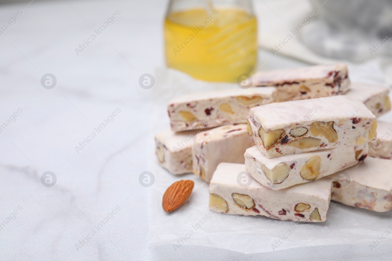 Photo of Pieces of delicious nutty nougat on white table, closeup. Space for text