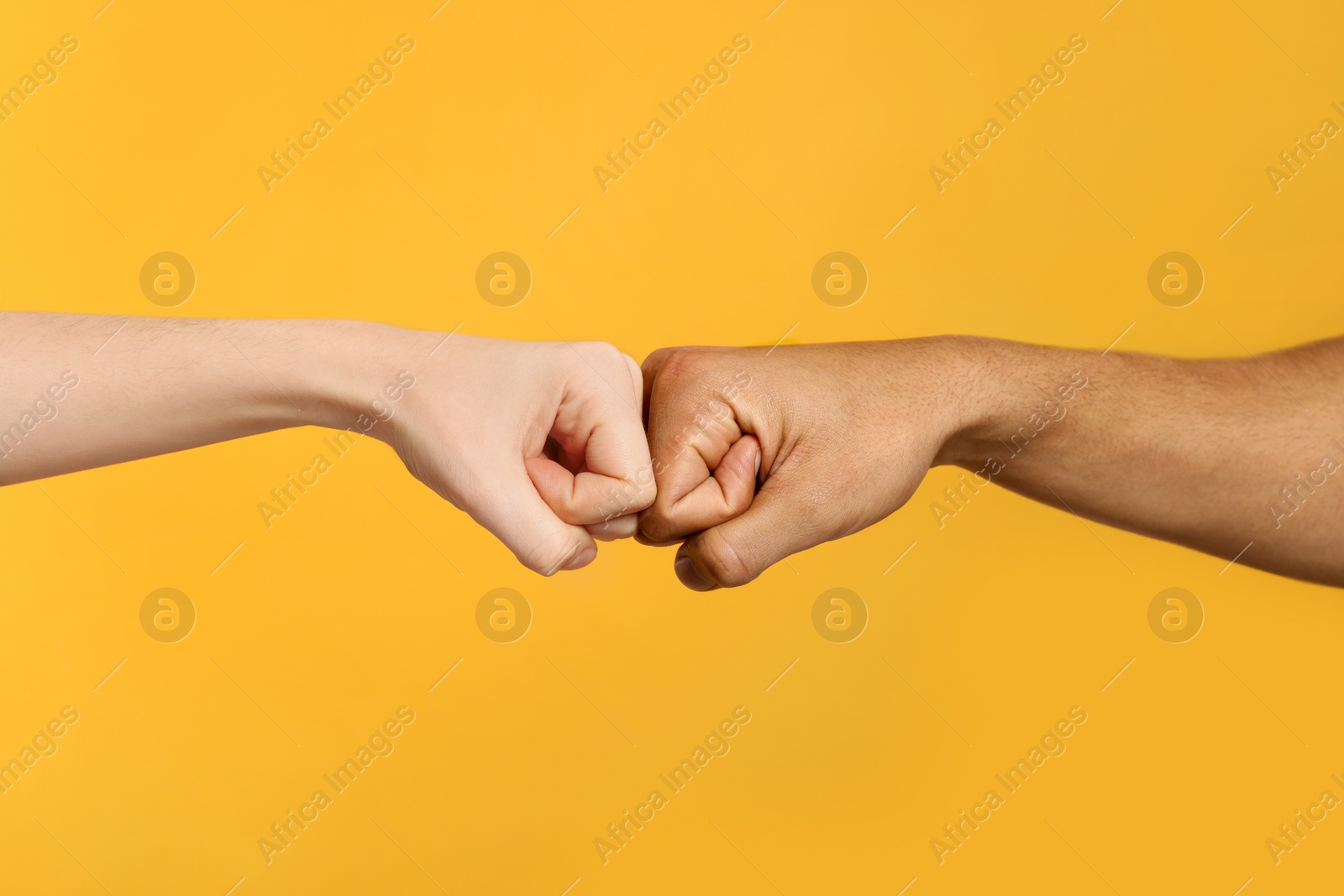 Photo of International relationships. People making fist bump on orange background, closeup