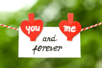 Photo of Romantic message. Card with You And Me Forever text made of paper hearts and clothespins outdoors