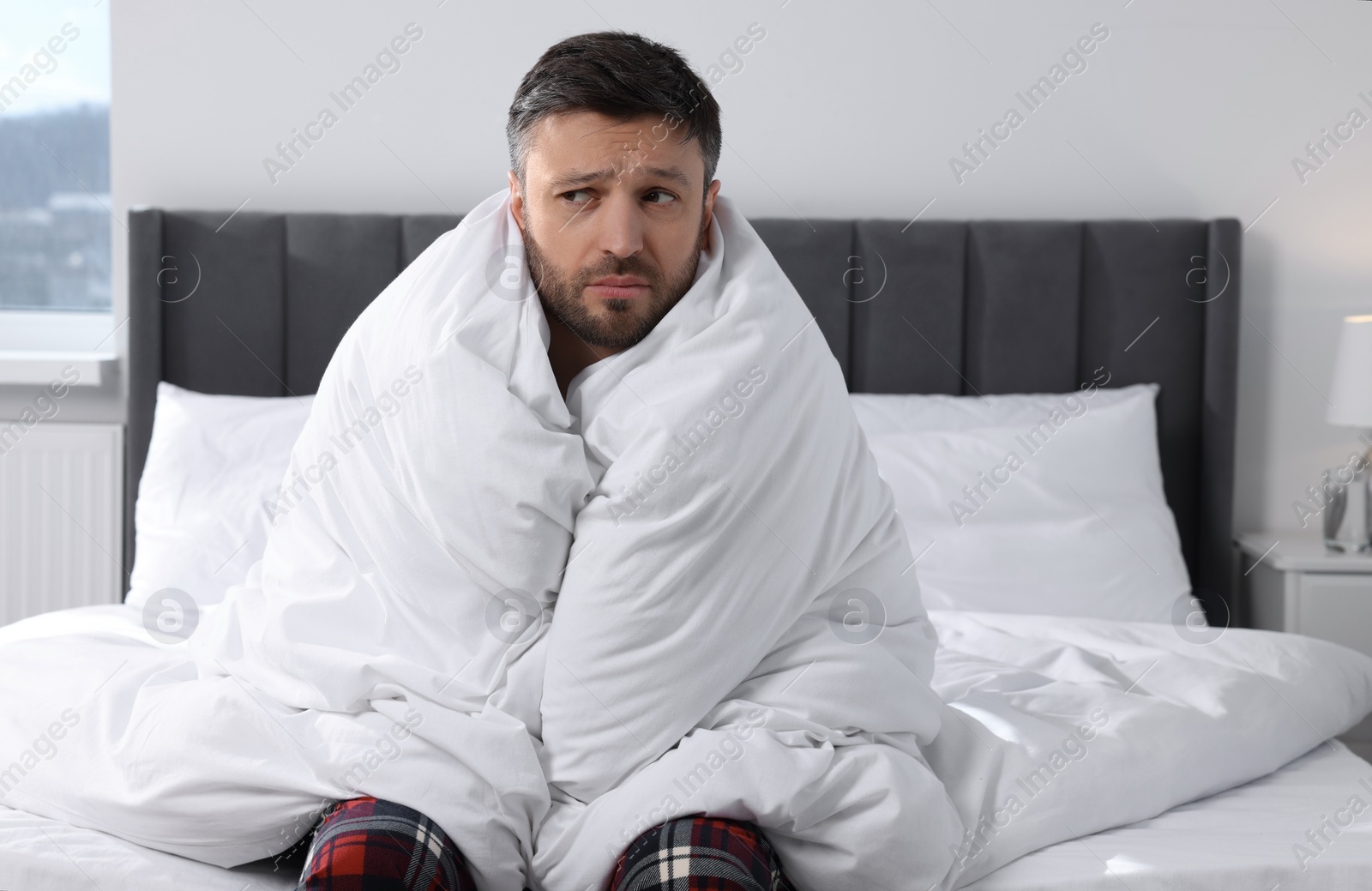 Photo of Sleepy man wrapped in blanket on soft bed at home in morning