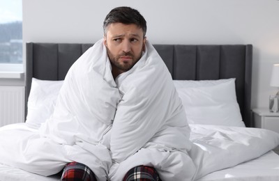 Photo of Sleepy man wrapped in blanket on soft bed at home in morning