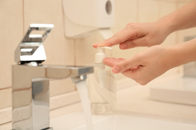 Photo of Woman applying antiseptic soap onto hand in bathroom, closeup. Virus prevention