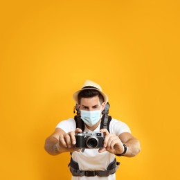Photo of Male tourist in protective mask with travel backpack taking picture against yellow background, focus on camera