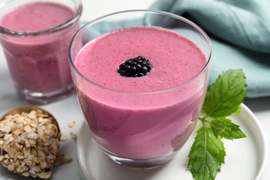 Photo of Glasses of blackberry smoothie with mint and oatmeal on white table, closeup