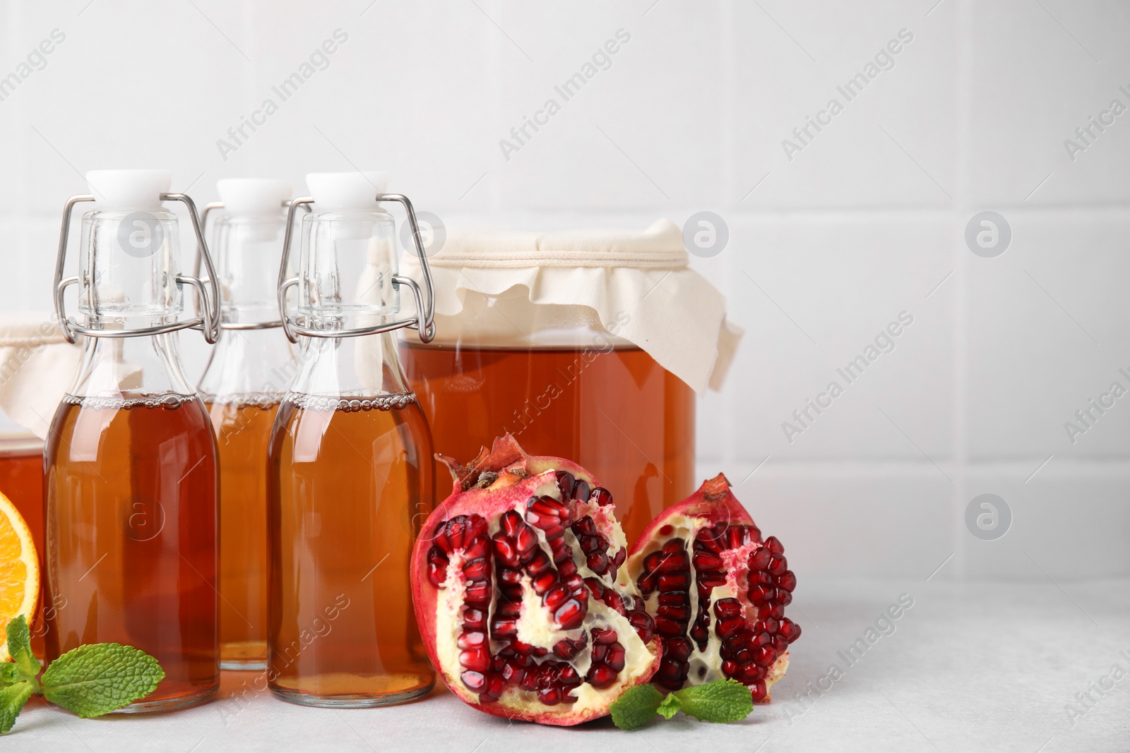 Photo of Tasty kombucha, pomegranate and mint on white table, space for text