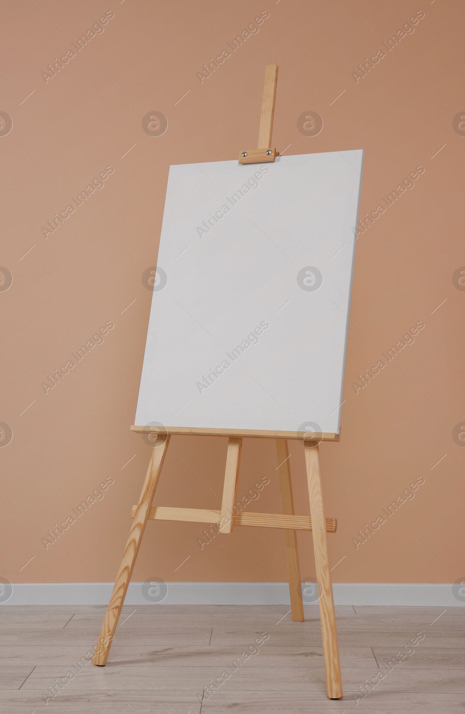 Photo of Wooden easel with blank canvas near beige wall indoors