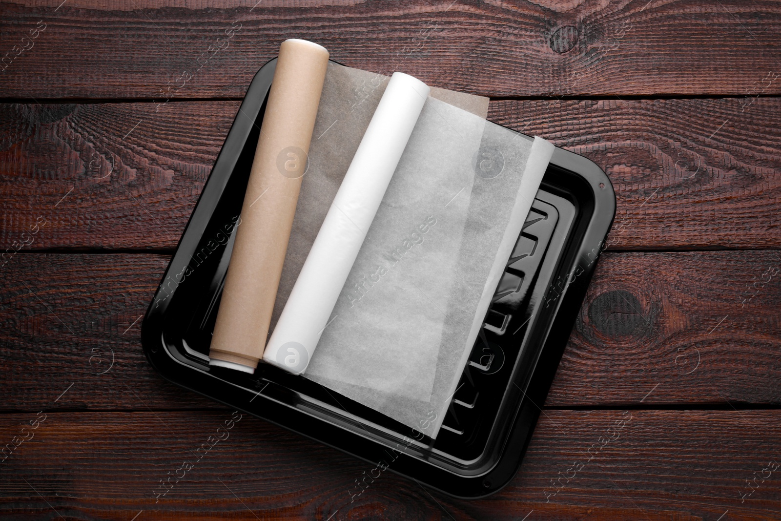 Photo of Baking pan with rolls of parchment paper on wooden table, top view