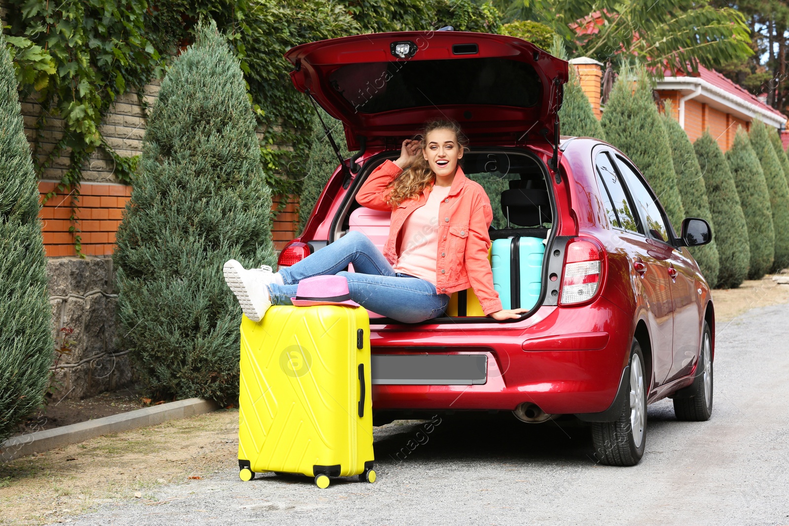 Photo of Beautiful young woman sitting in car trunk loaded with suitcases outdoors