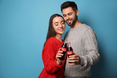 Photo of MYKOLAIV, UKRAINE - JANUARY 27, 2021: Young couple holding bottles of Coca-Cola on light blue background. Space for text