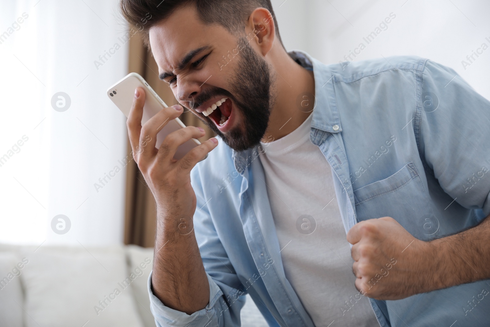 Photo of Emotional young man talking on mobile phone at home. Hate concept