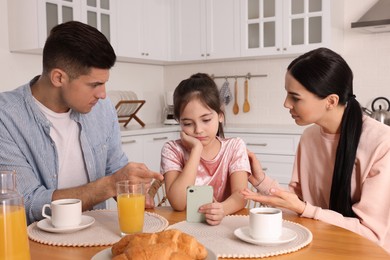 Photo of Internet addiction. Parents scolding their daughter while she using smartphone at table in kitchen